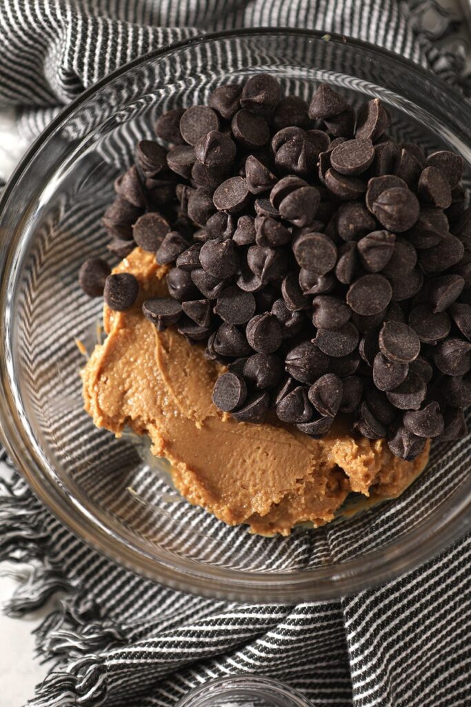 Peanut butter and chocolate chips together in a glass bowl on top of a gray and white towel