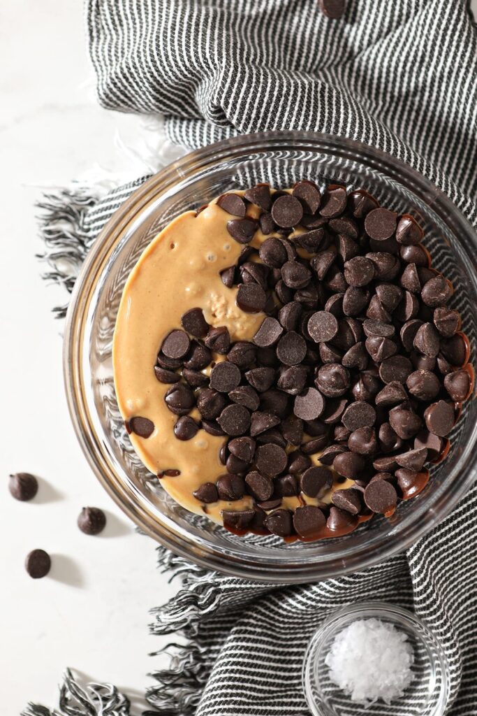 Melted peanut butter and chocolate chips together in a glass bowl on top of a gray and white towel