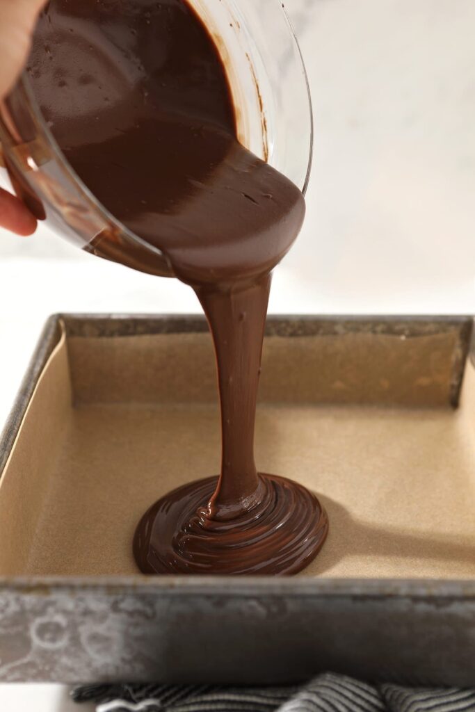 The chocolate-peanut butter mixture pours into a parchment-lined baking dish