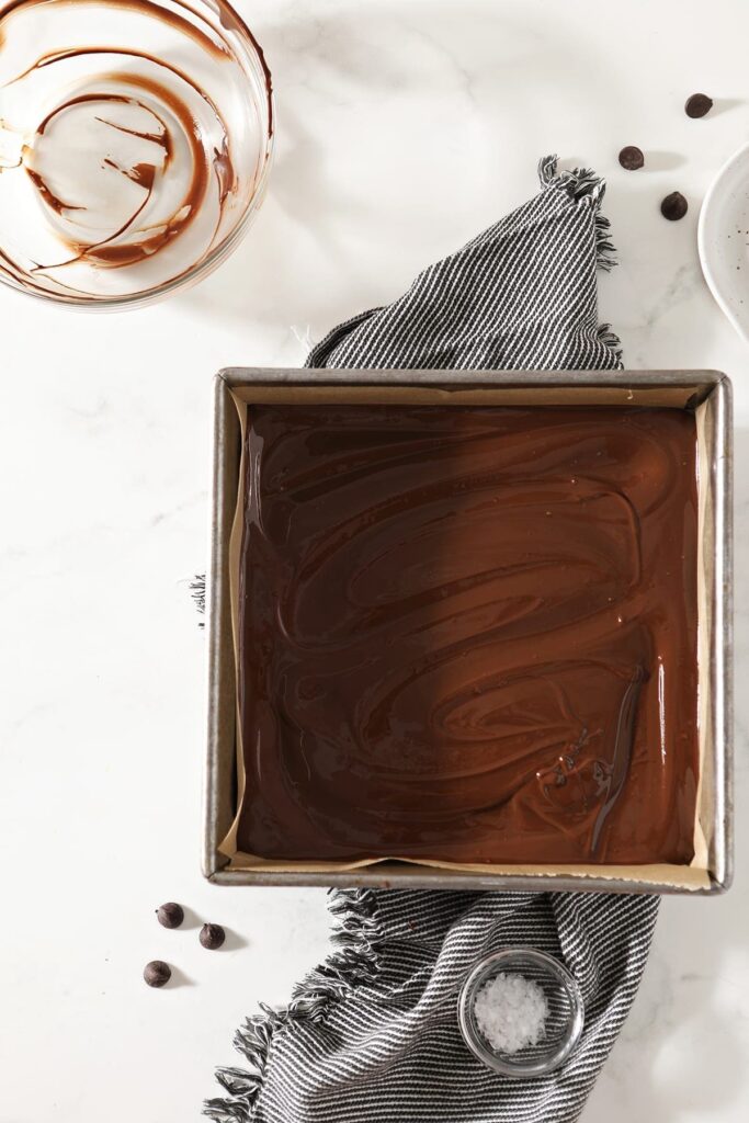 The fudge in a baking dish, on top of a gray and white striped towel