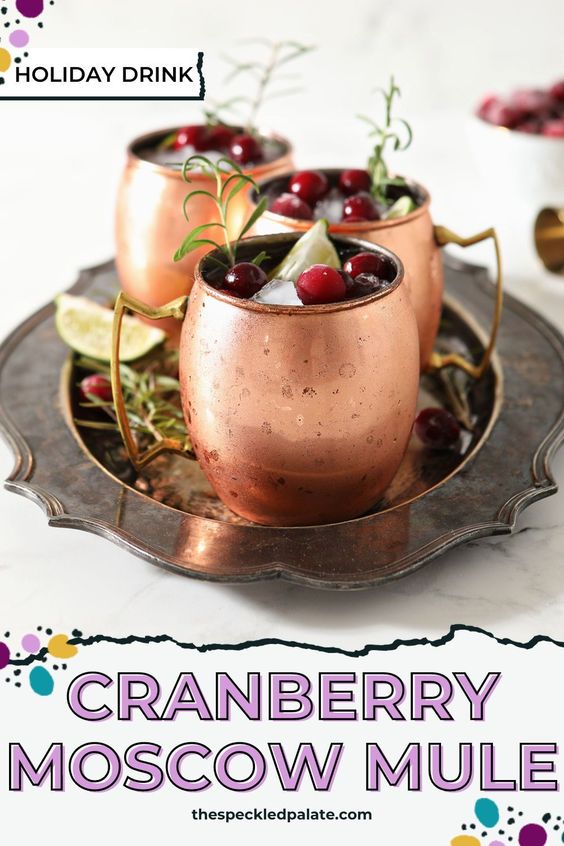 Three Yule Mules, garnished with fresh cranberries, lime wedges and rosemary sprigs, sit on a silver platter with the text 'cranberry moscow mule'