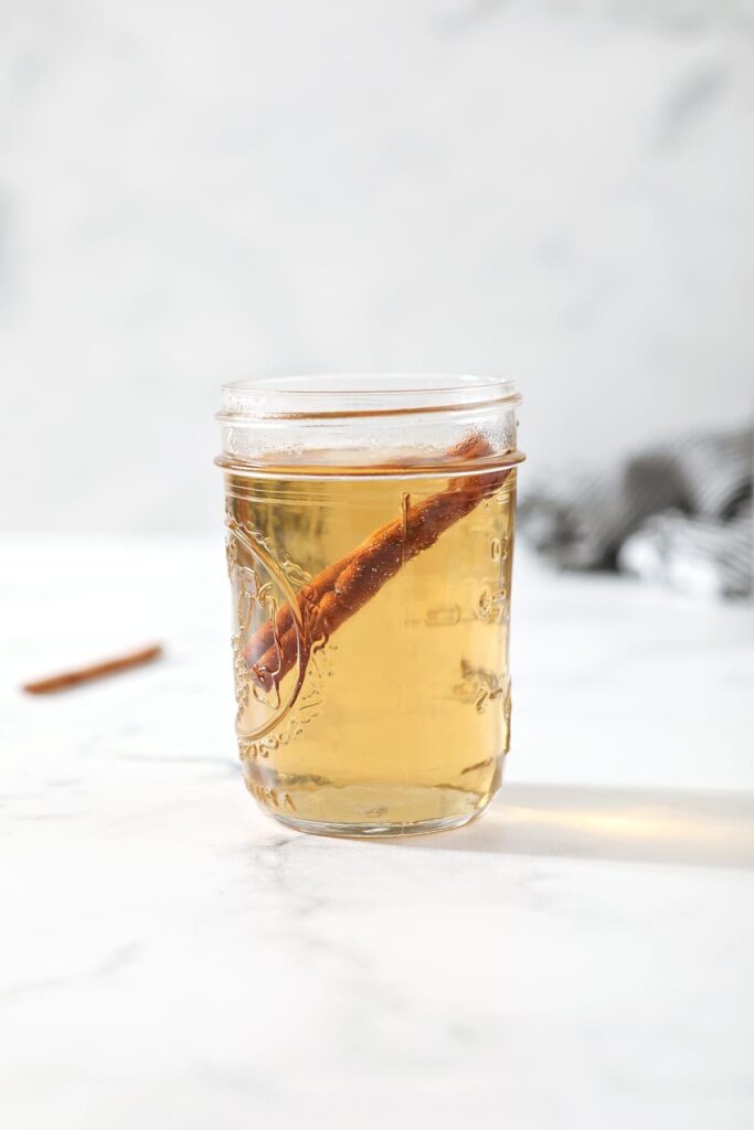 A jar holds simple syrup with cinnamon in it on a marble countertop