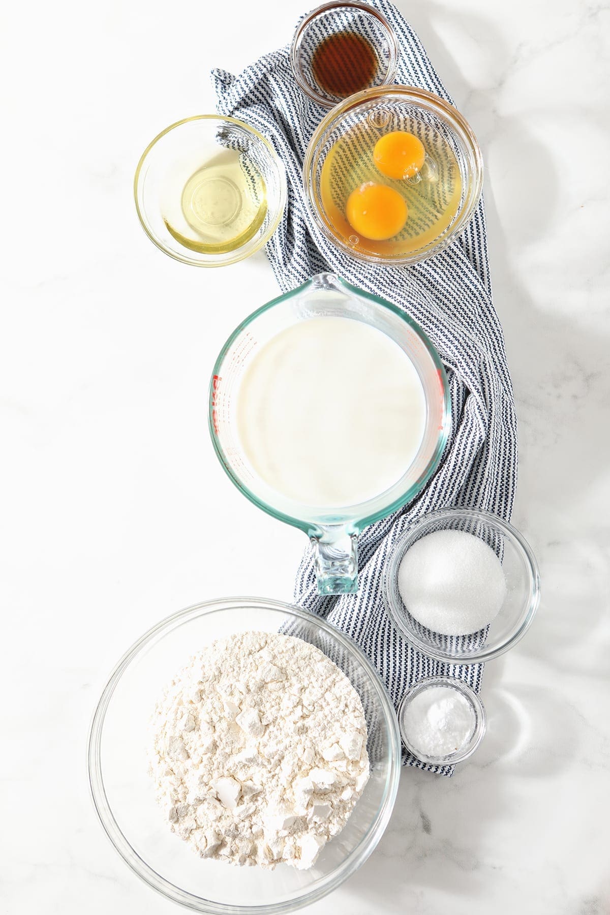 Bowls of ingredients sit on a blue striped towel on a marble counter