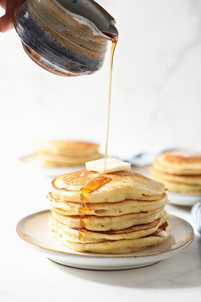 Syrup pours onto a stack of fluffy homemade pancakes