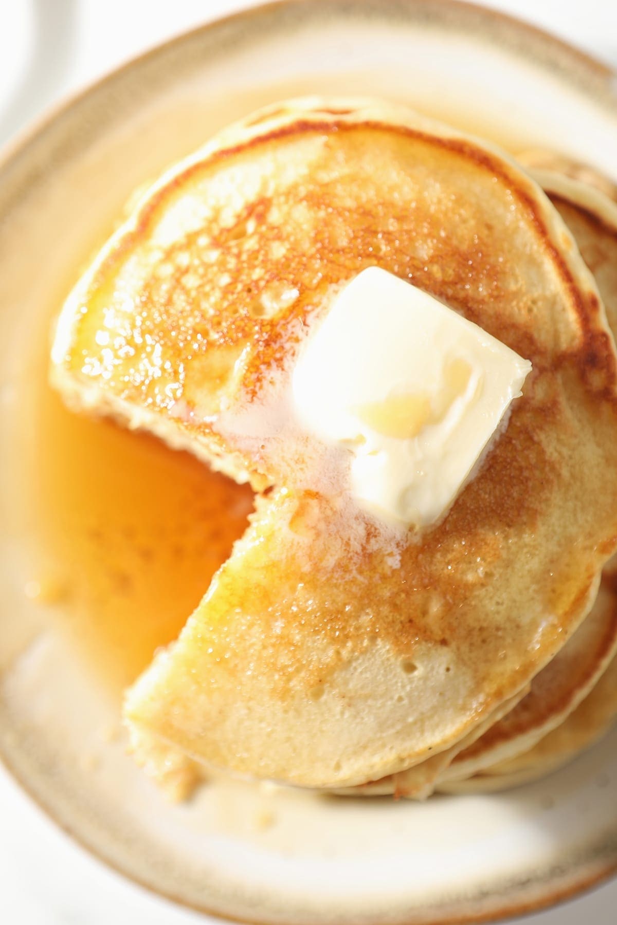 Close up of a stack of pancakes, with a wedge cut out of it, with butter and syrup on top