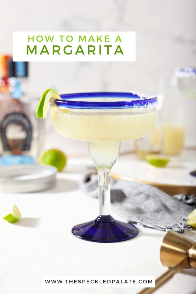 A margarita sits on a marble counter in front of ingredients with the text 'how to make a margarita'