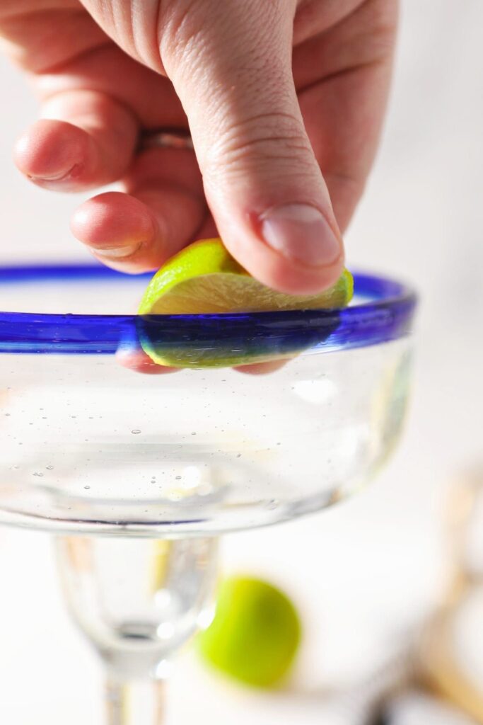 A lime runs along the edge of a blue-rimmed margarita glass