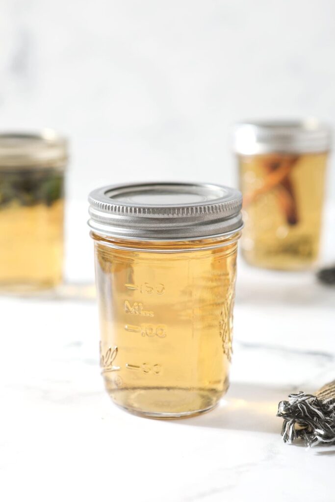 A mason jar holding regular simple syrup sits on front of two other jars holding mint simple syrup and cinnamon simple syrup on a marble surface