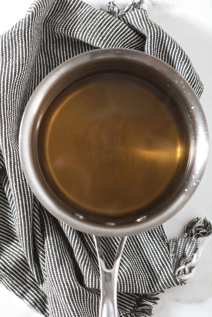 Simple syrup in a saucepan sits on top of a gray and white striped towel