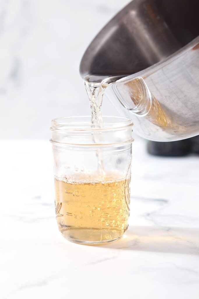 pouring simple syrup from a pot into a glass jar