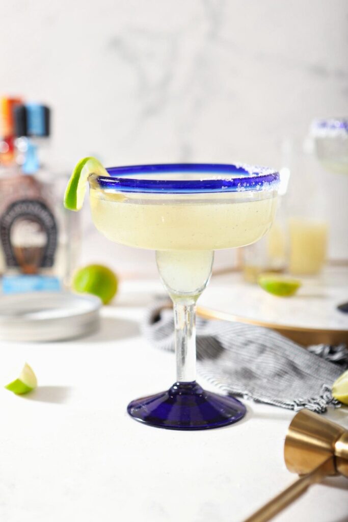 A margarita sits on a marble counter in front of ingredients