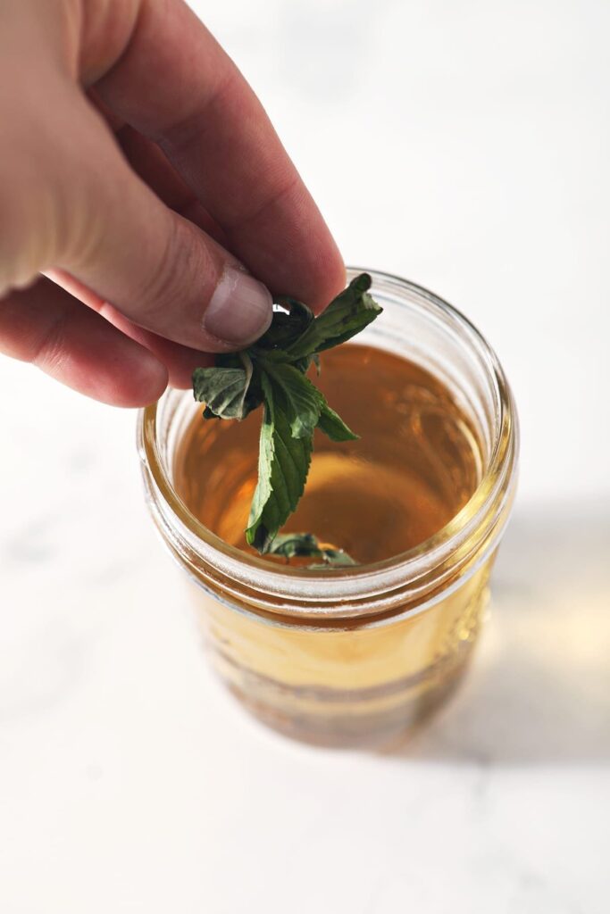 A person adds mint leaves to a jar of simple syrup