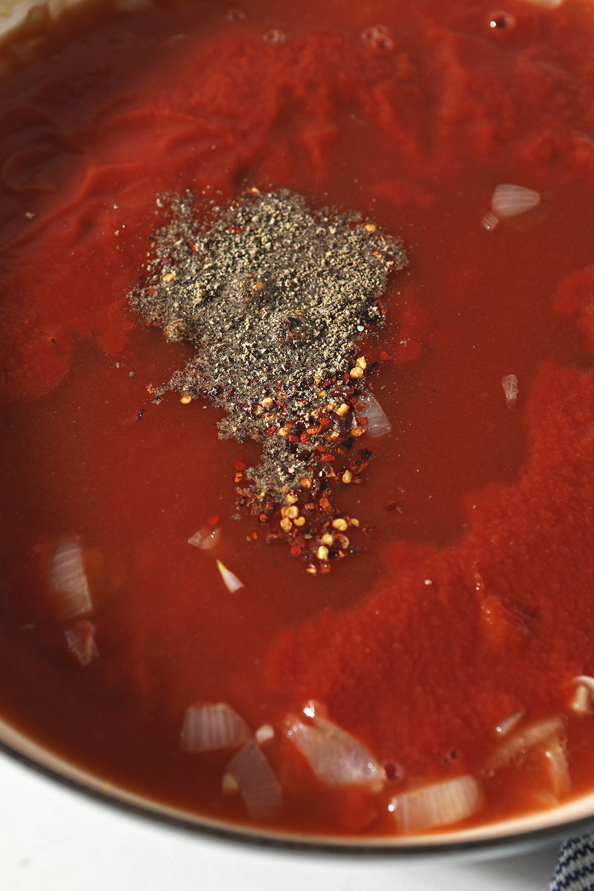 seasonings sit on top of a braiser pan of tomato sauce and other ingredients to make soup
