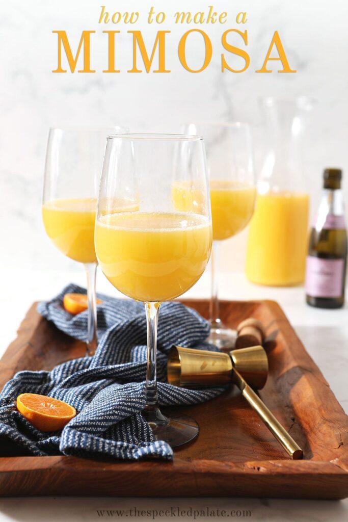 Three mimosas sit on a wooden tray with a dark blue towel with the text 'how to make a mimosa'