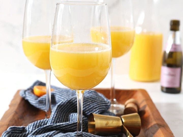 Three mimosas sit on a wooden tray with a dark blue towel