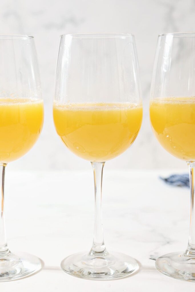 Three wine glasses holding orange drinks sit on a marble countertop