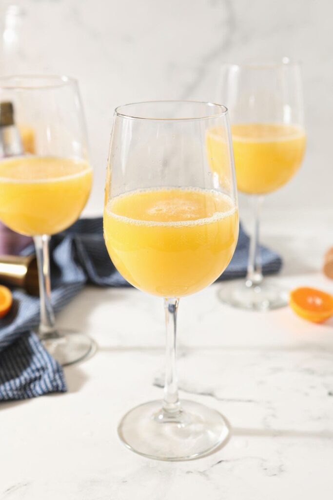 A classic mimosa in a wine glass sits in front of two more on a marble countertop