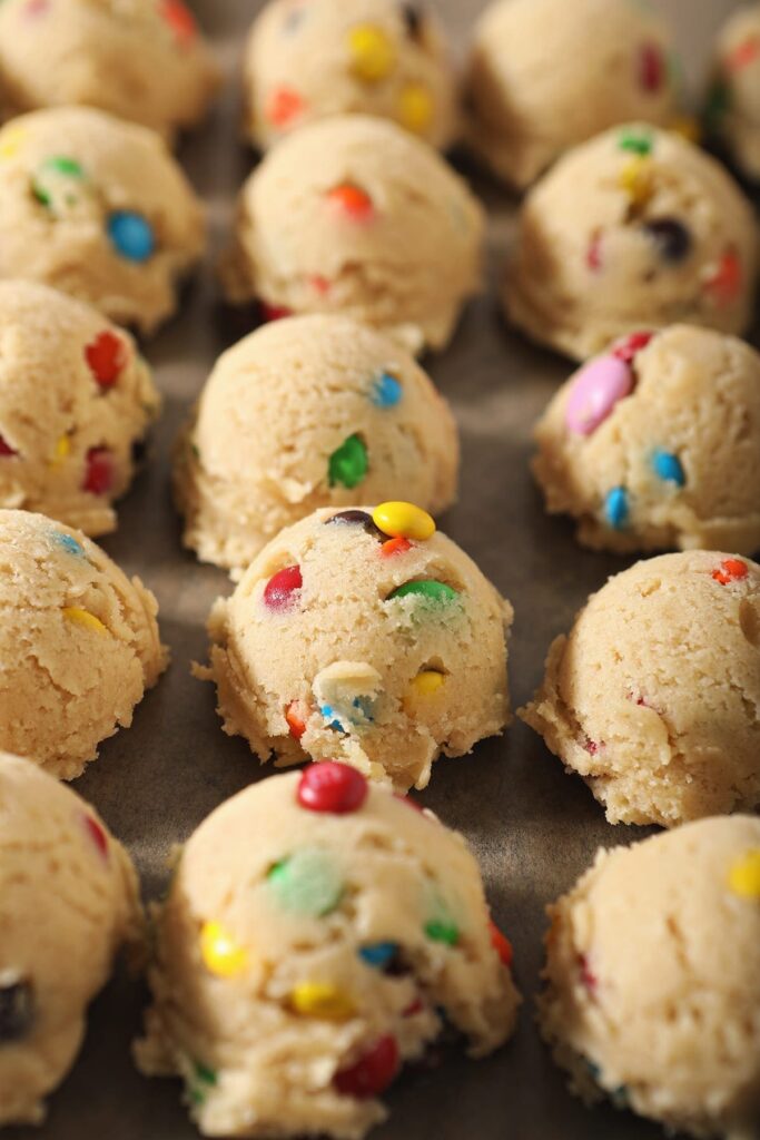 Dough balls full of M&Ms sit on a baking sheet before freezing