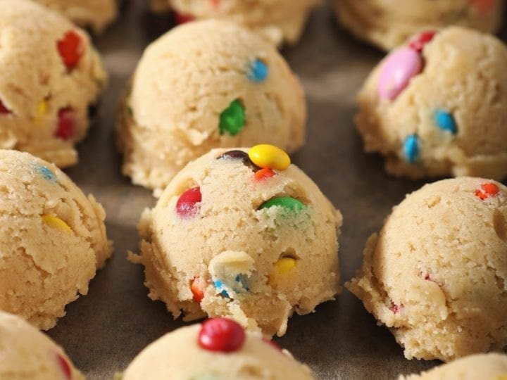 Dough balls full of M&Ms sit on a baking sheet before freezing