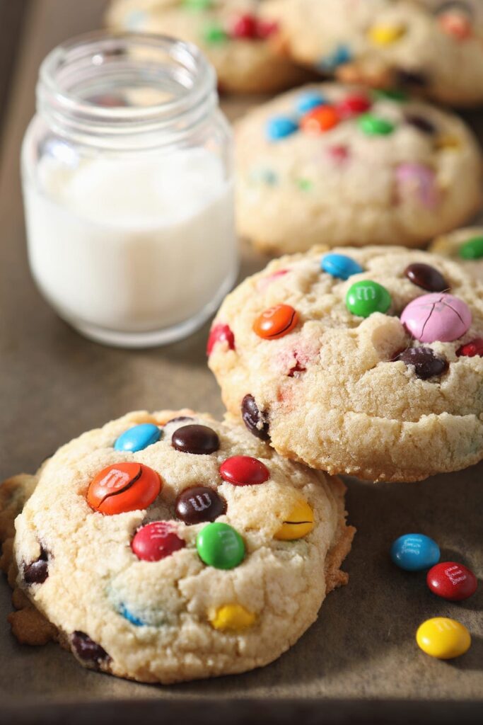 Stacked cookies sit next to a glass of milk on a baking sheet