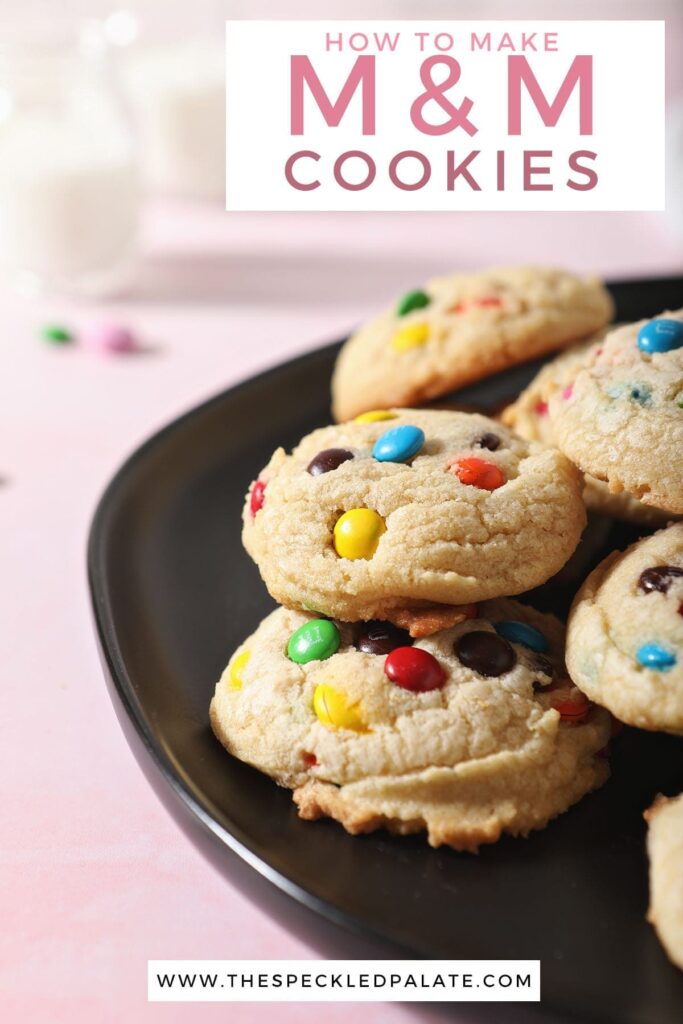 A black plate holds stacked cookies on a pink surface with the text 'how to make m&m cookies'