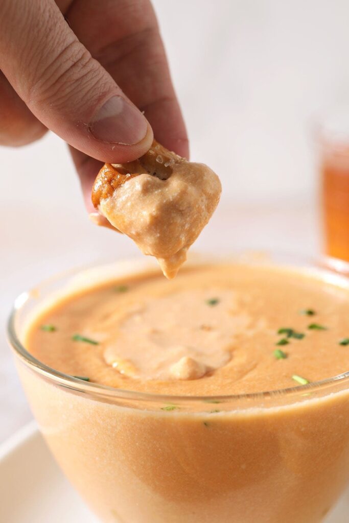 A person dips a pretzel bite into a bowl of cheese sauce