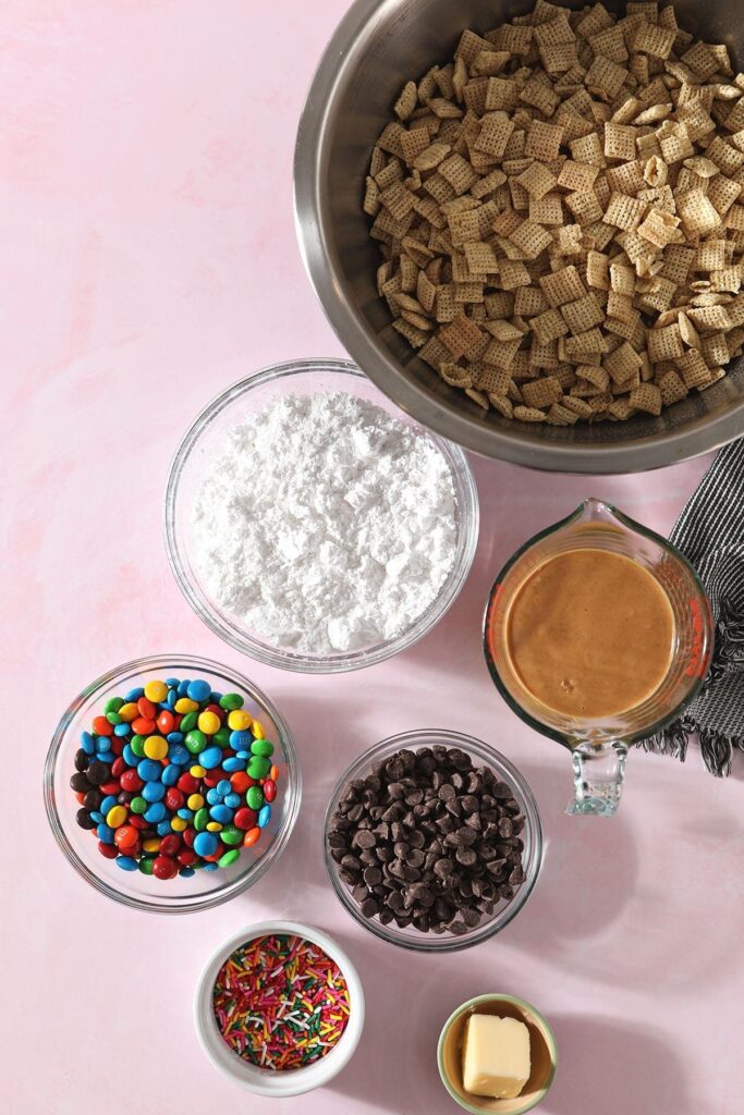 Ingredients for Chex Mix Puppy Chow in bowls on a pink countertop