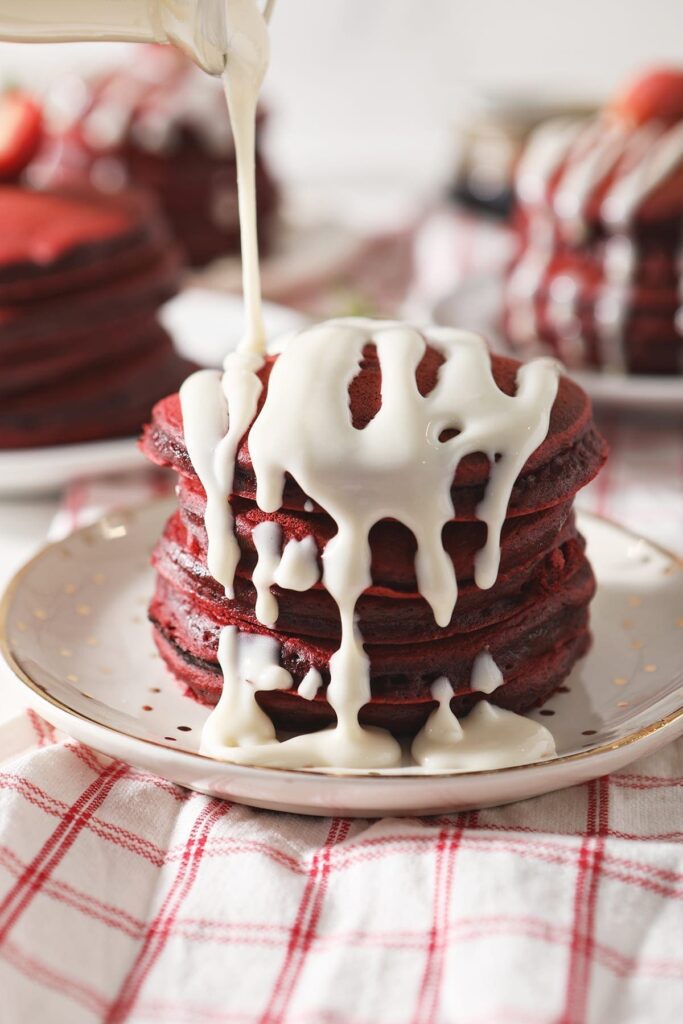 A cream cheese glaze drizzled onto a stack of red velvet pancakes