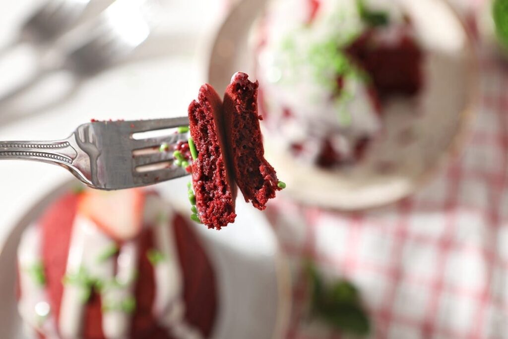 A fork spears pieces of red velvet pancakes and their garnishes above a table holding plates of the pancakes