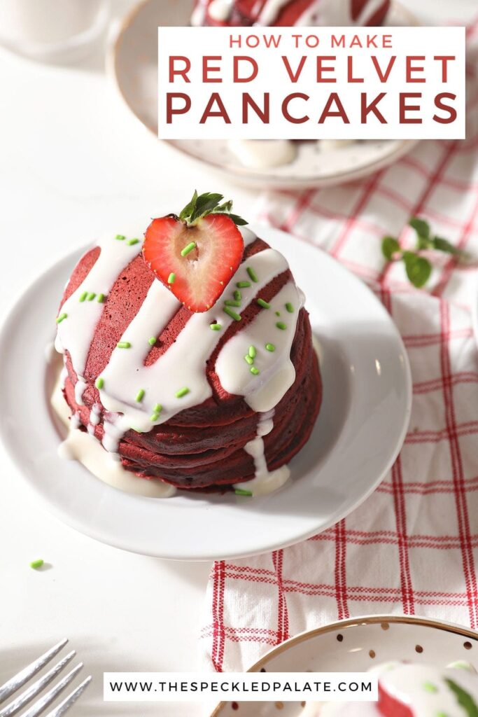 A stack of red velvet pancakes is garnished with a cream cheese glaze, green sprinkles and a halved strawberry on a white plate with the text 'how to make red velvet pancakes'