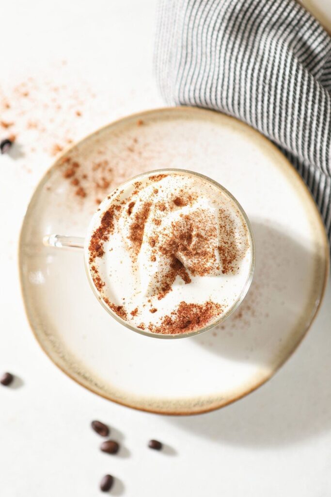 Overhead of a drink topped with whipped cream and sprinkled cinnamon sitting on a plate