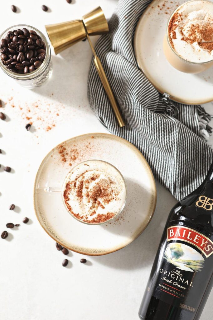 Two plates holding mugs of coffee drinks from above next to coffee beans and a jigger