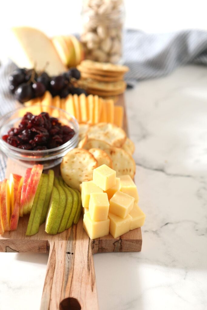 Stacked cheese cubes next to sliced fruit on a board