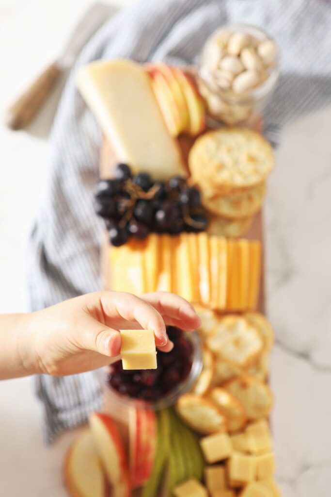 A child holds a cube of cheese above a snack board