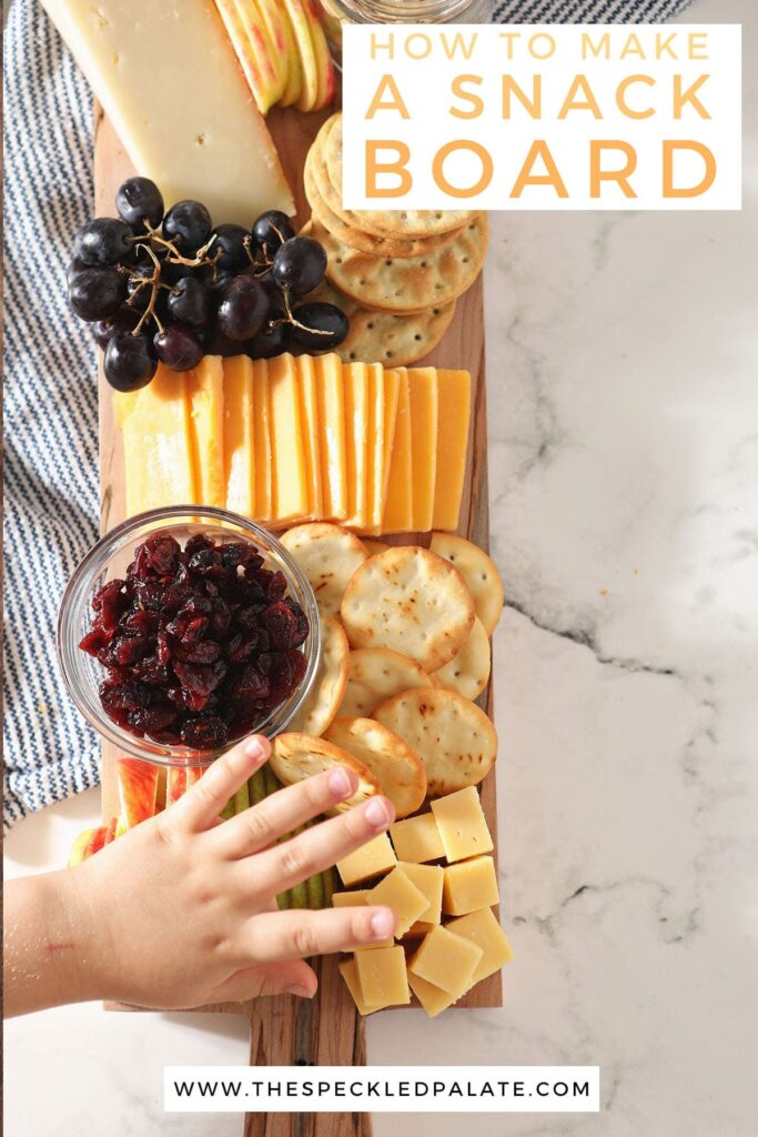 A child reaches for cubed cheese on a wooden board with the text 'how to make a snack board'