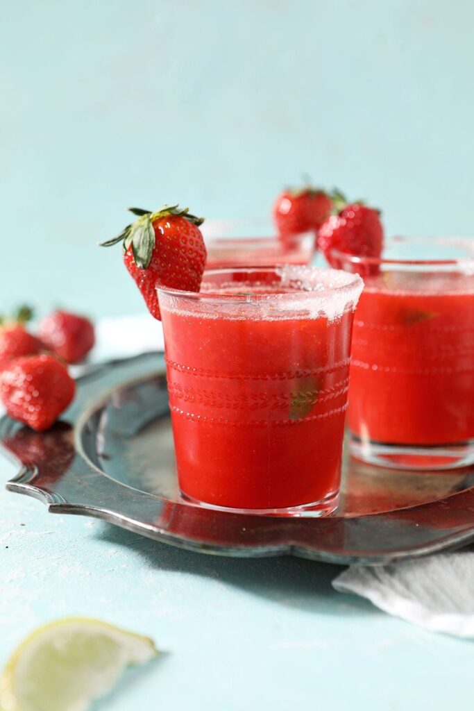 A silver tray holds three red drinks garnished with strawberries