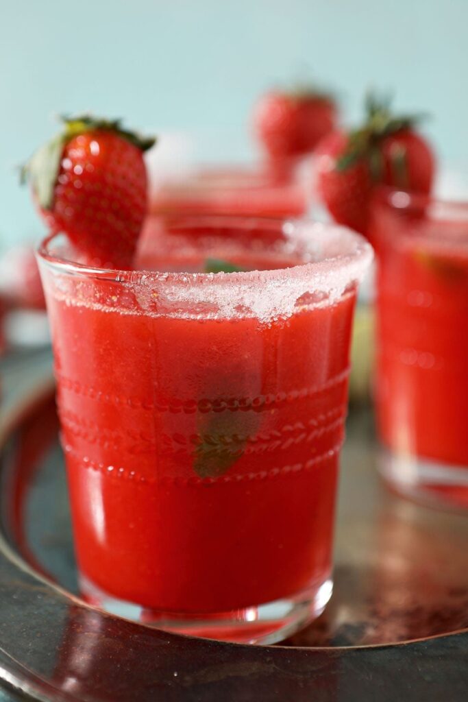 Close up of a strawberry margarita rimmed with sugar and garnished with a strawberry and a lime wedge