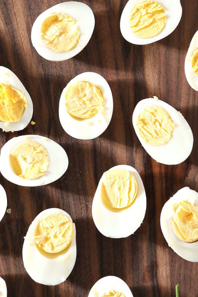 Several halved hard boiled eggs sit on a dark wooden cutting board