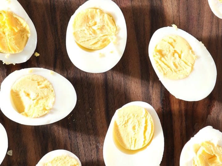 Several halved hard boiled eggs sit on a dark wooden cutting board