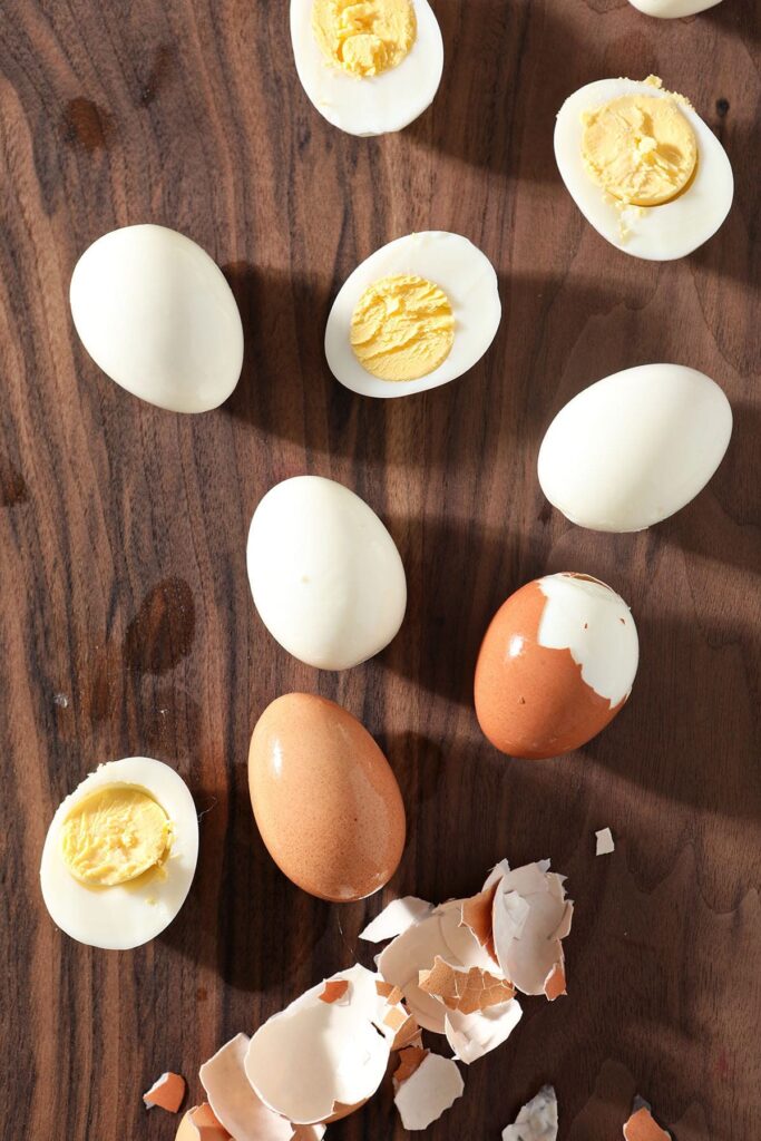 Hard boiled eggs are peeled on a dark wood cutting board