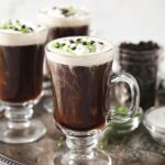 Three Irish Coffees sit on a silver tray, garnished with whipped cream, chocolate and green sprinkles