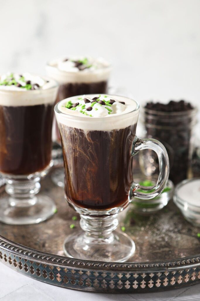 Three Irish Coffees sit on a silver tray, garnished with whipped cream, chocolate and green sprinkles