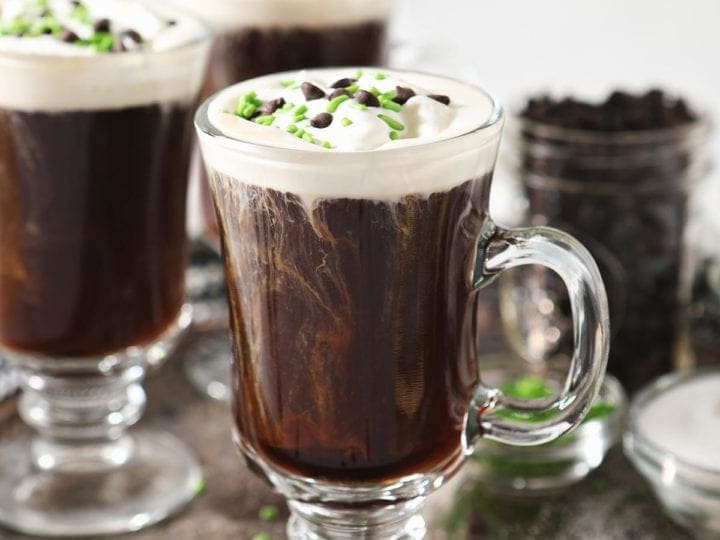 Three Irish Coffees sit on a silver tray, garnished with whipped cream, chocolate and green sprinkles