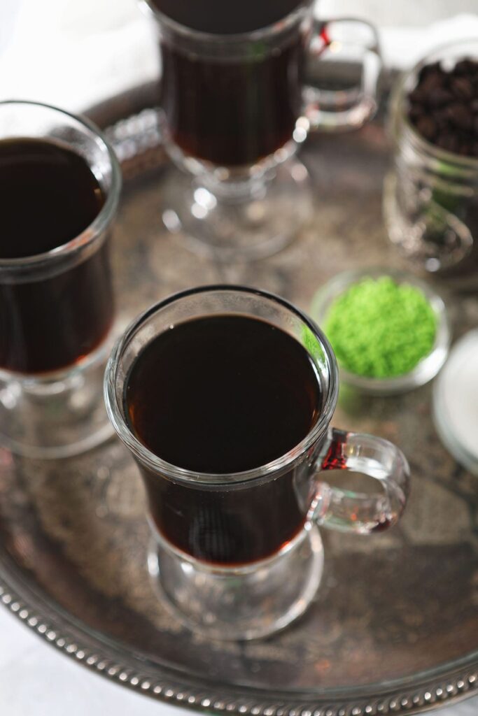 Three Irish Coffee glasses hold sweetened coffee on a silver tray