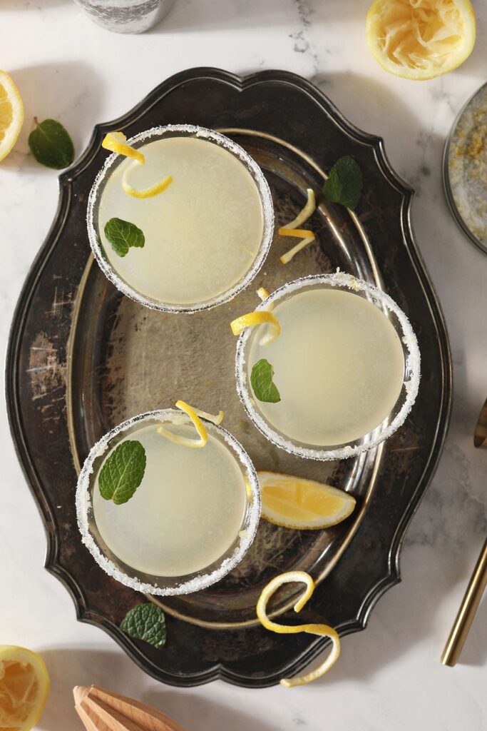 Three Lemon Drop Martinis garnished with mint leaves and lemon twists sit on a silver tray