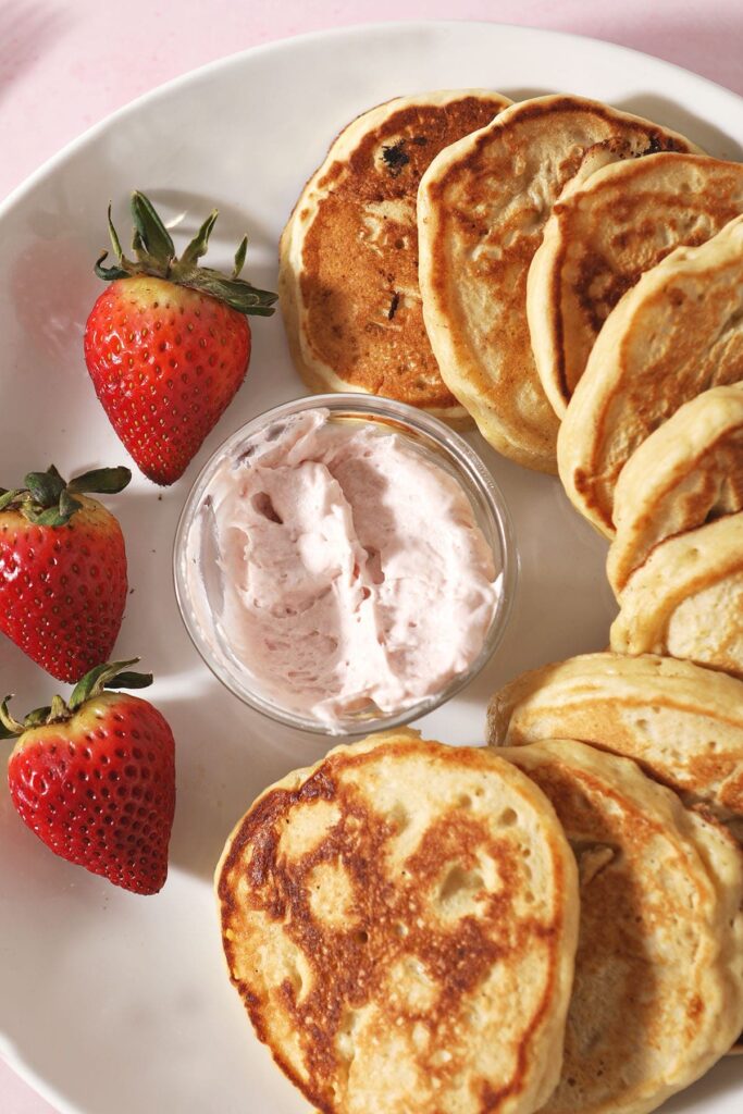 A plate of pancakes circles around a bowl of strawberry whipped cream with fresh strawberries