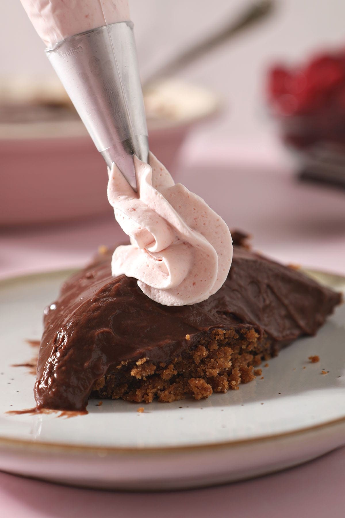 A piping bag pipes whipped cream onto a slice of chocolate pie