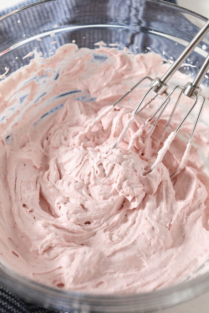 Whisks in a bowl of strawberry whipped cream