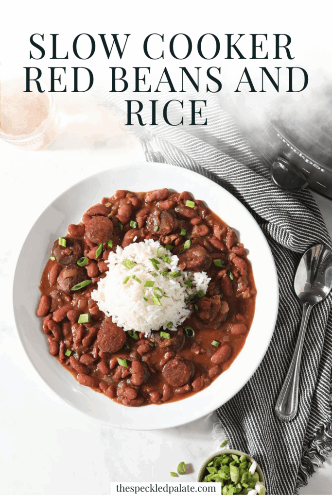 A bowl of Slow Cooker Red Beans and Rice sits next to a glass of beer and a slow cooker