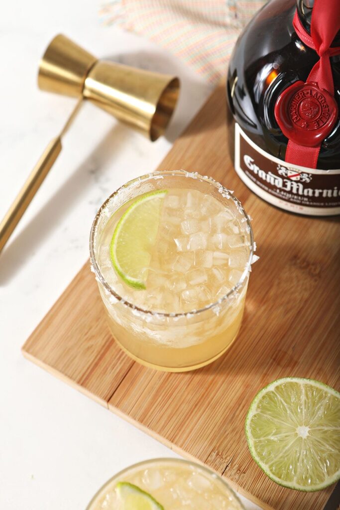 A margarita garnished with a lime sits next to a bottle of Grand Marnier